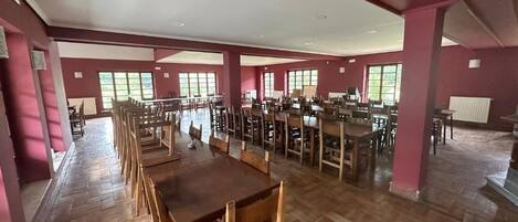 A spacious dining area with multiple tables and chairs, large windows, and a herringbone floor pattern.