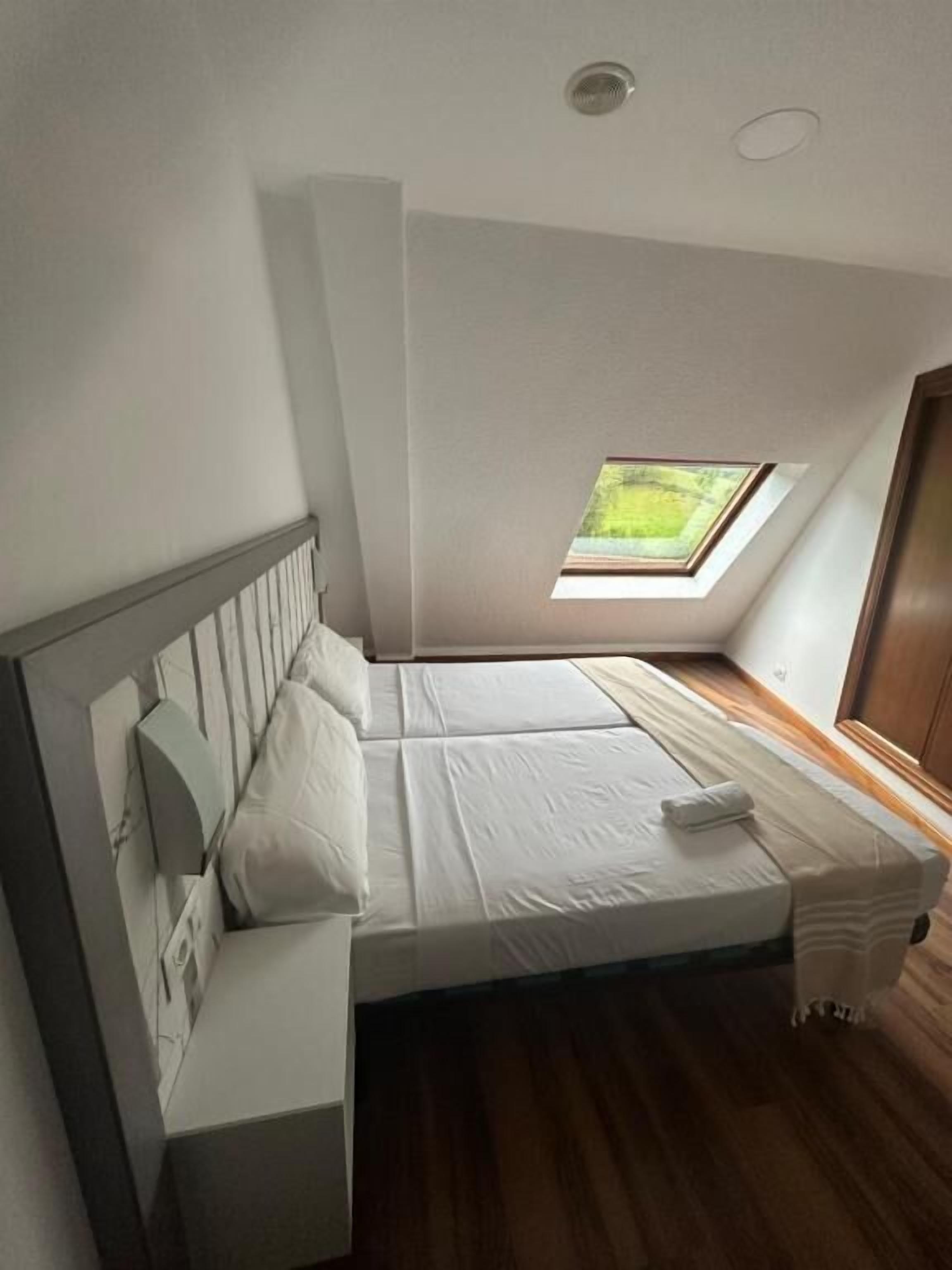 A bedroom with a skylight, a bed, a bedside table, and a wooden floor.