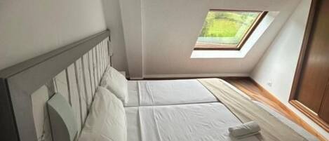 A bedroom with a skylight, a bed, a bedside table, and a wooden floor.