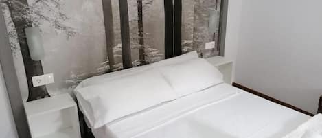 Una cama bien hecha con sábanas blancas en una habitación con un cabecero moderno y un papel tapiz con motivos de bosque.