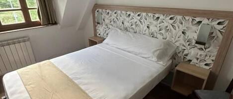 A neatly made bed with a wooden headboard and a beige throw blanket.