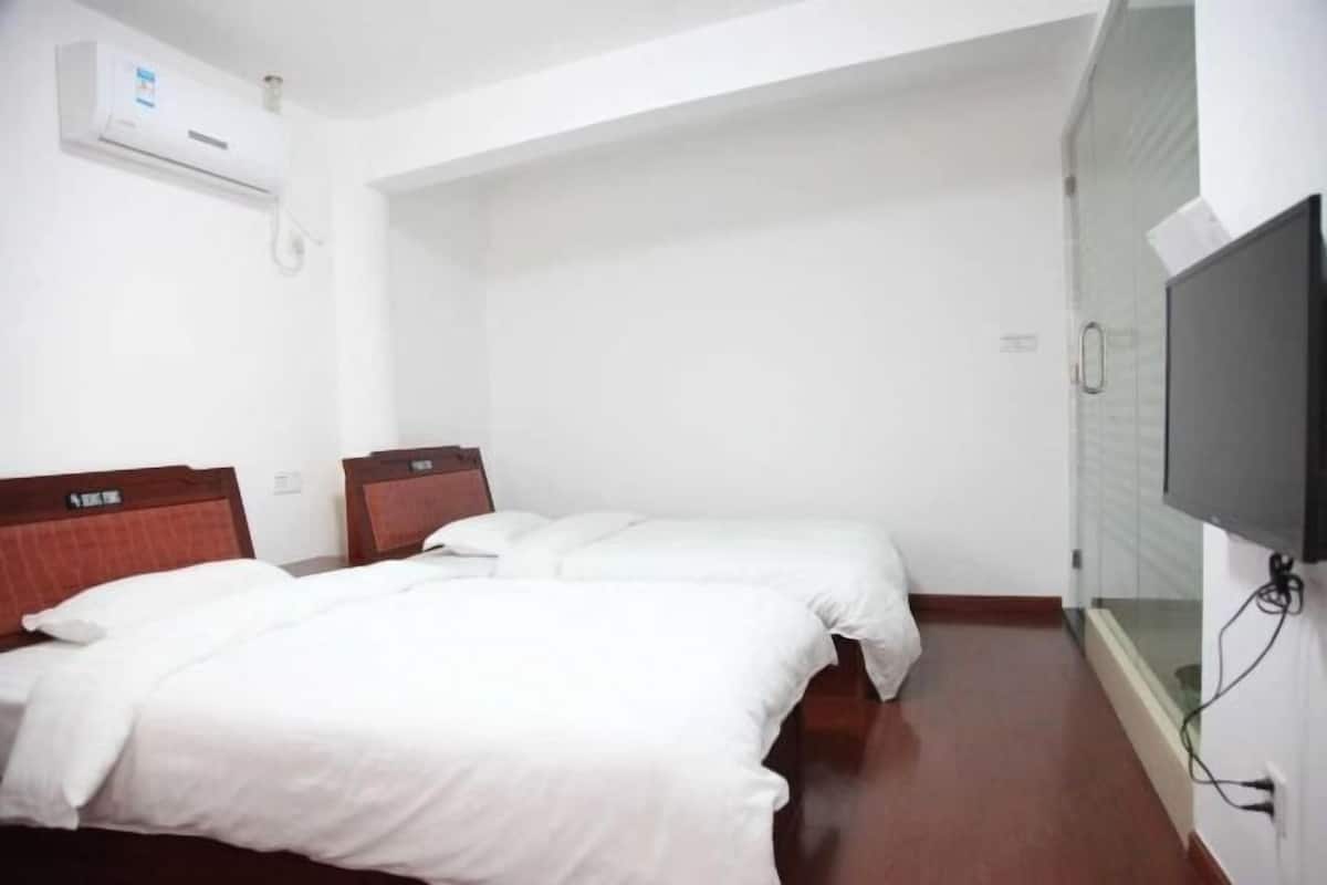 A hotel room with two beds, a TV, and an air conditioning unit.