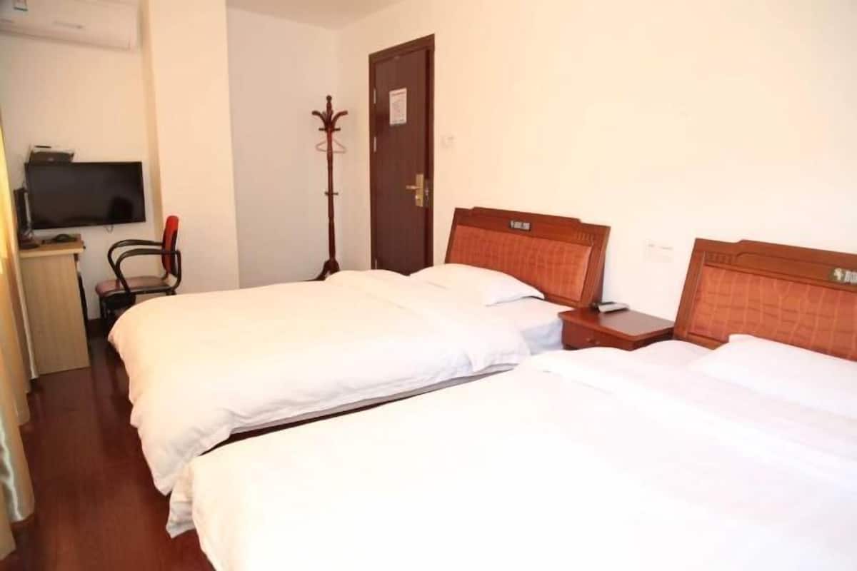 A hotel room with two single beds, a television, a coat rack, and a door.