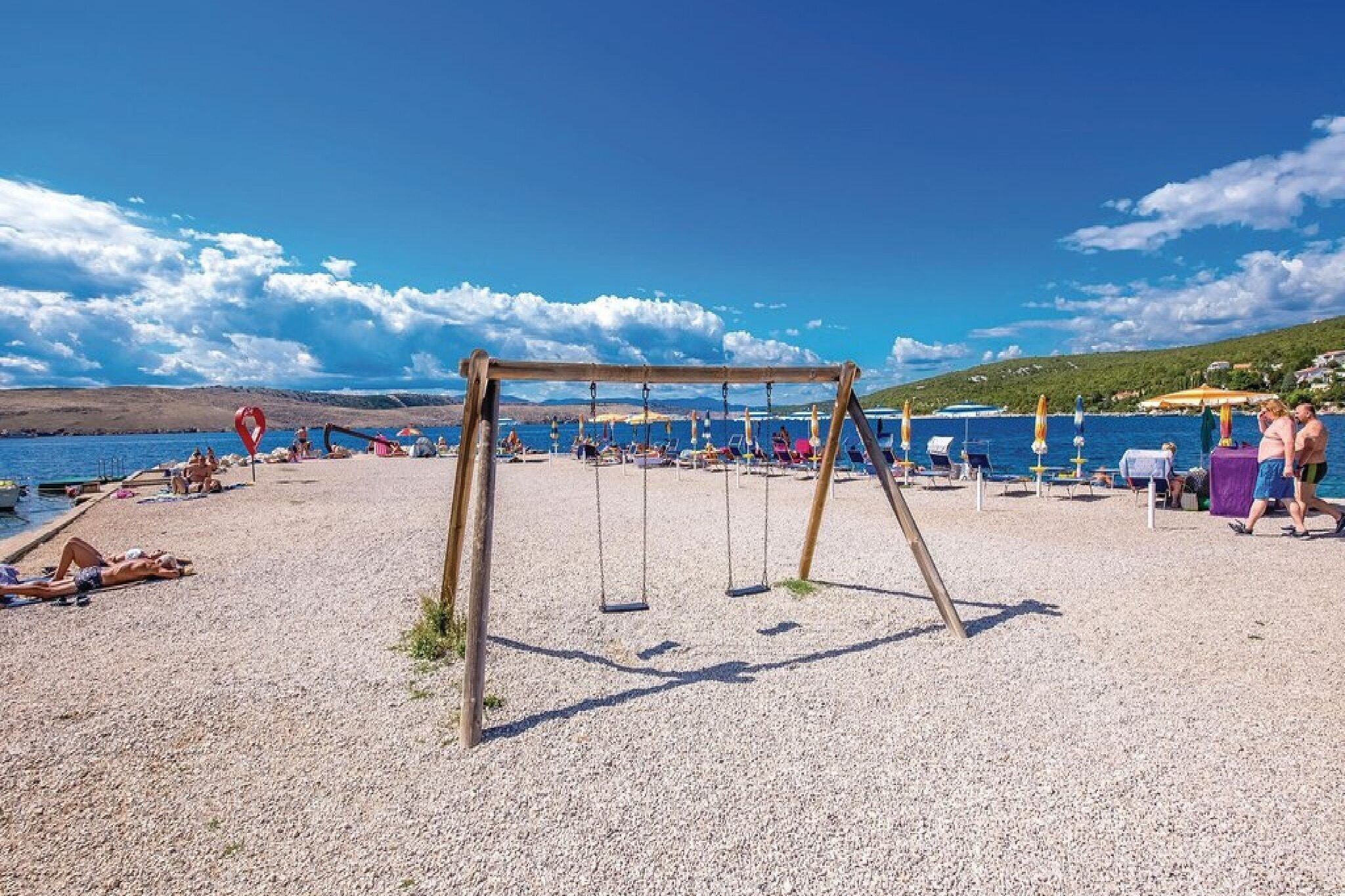 Une plage avec des balançoires, des chaises longues et des parasols.
