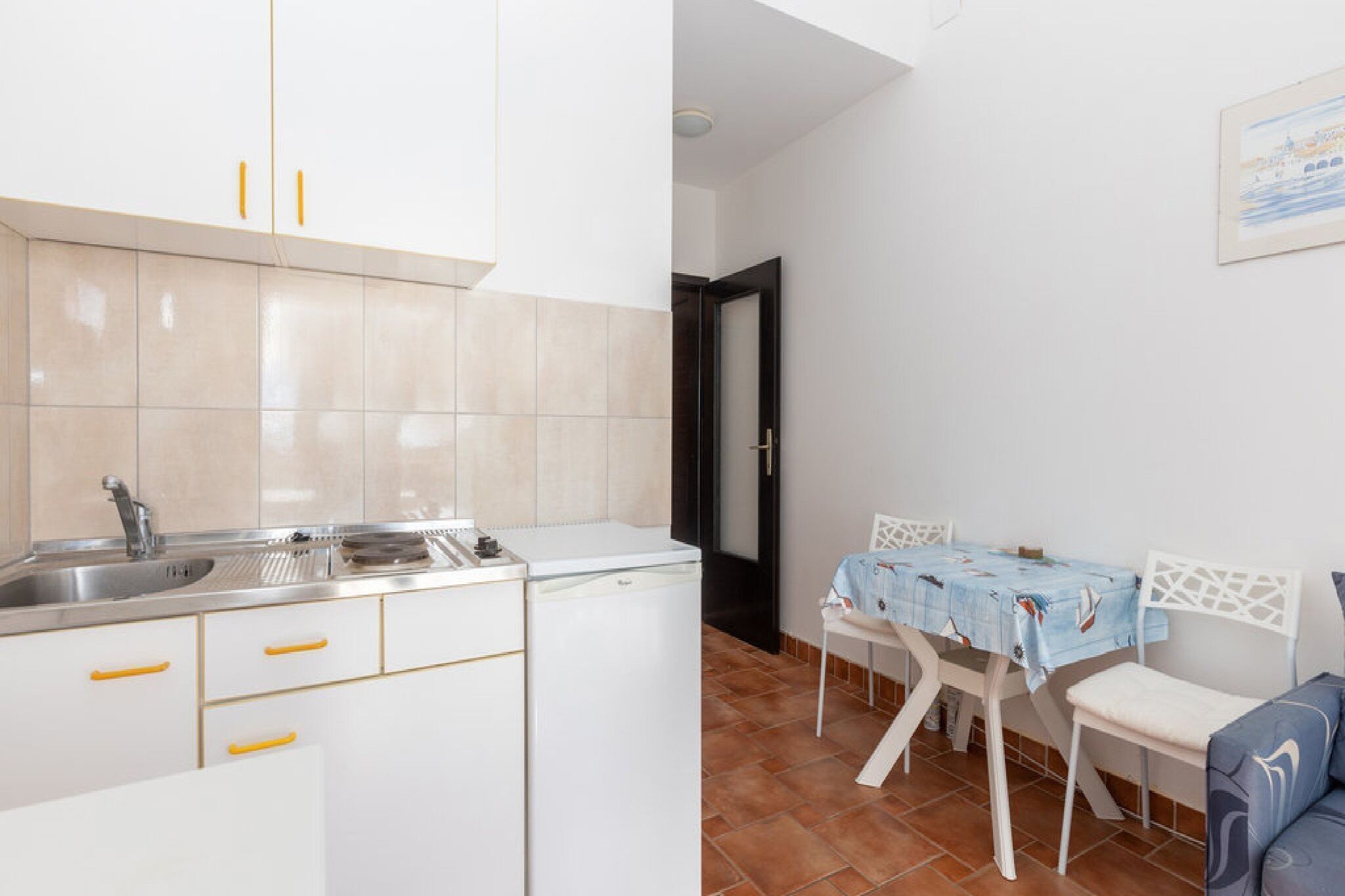 A kitchen with white cabinets and a sink, a dining area with a table and chairs, and a door leading to another room.