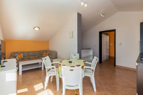 A modern living room with a sofa, coffee table, and dining table with chairs. There is a kitchen area with cabinets and a countertop. - Apartments Ilija Njavro - One Bedroom Apartment with Terrace and Sea View (Jadranovo)
