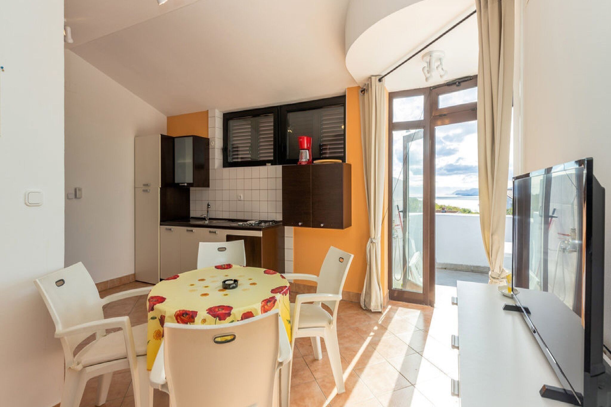 Cocina compacta con comedor, televisor y balcón con vistas.
