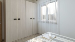 A bedroom with a bed, a wardrobe, and a window with sheer curtains.