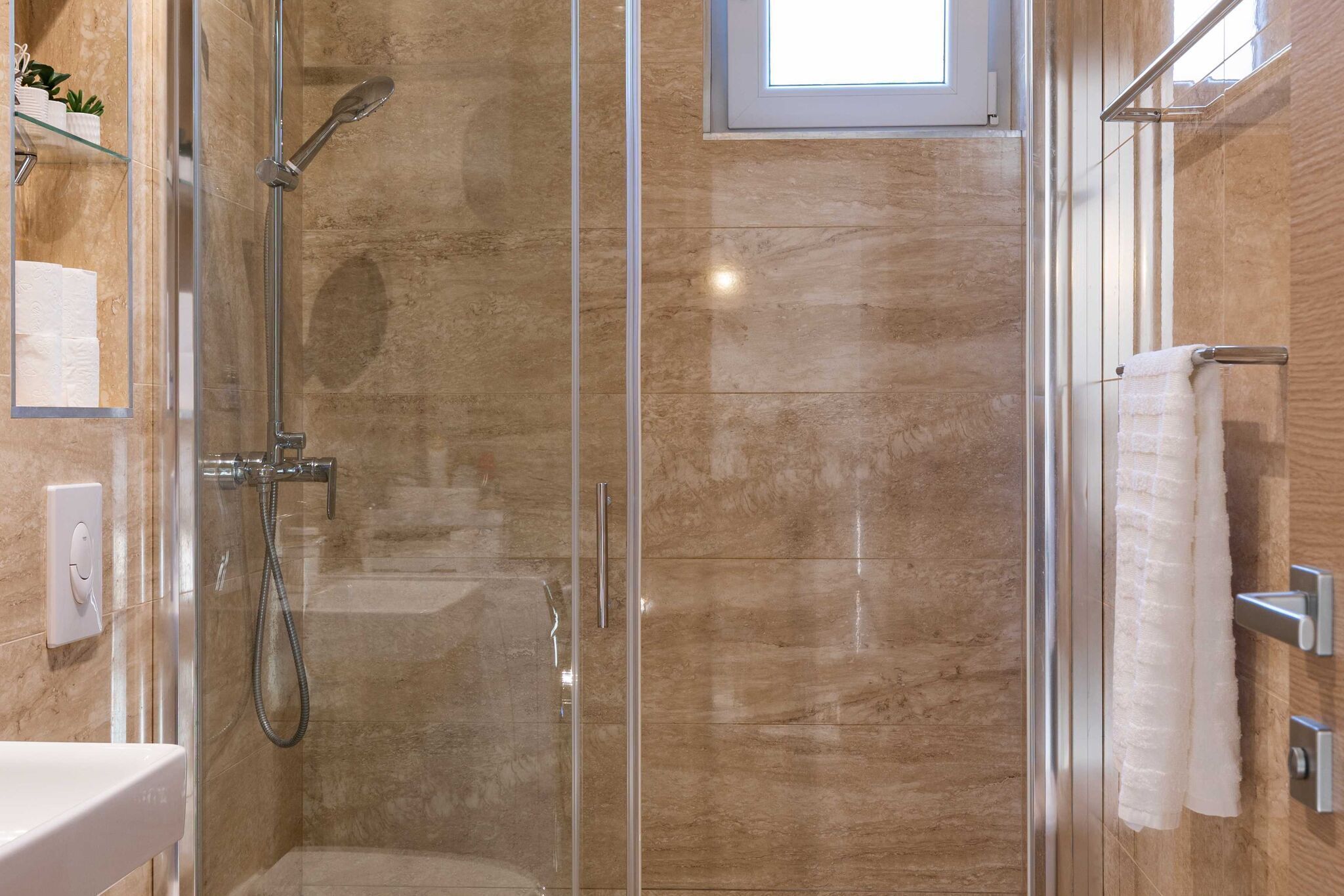A glass-enclosed shower with a handheld showerhead and a wall-mounted faucet.