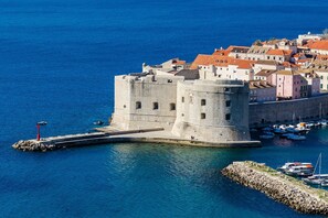 A historic stone fortress with a moat, surrounded by colorful buildings and boats in the water.