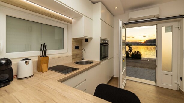 A modern kitchen with a view of a sunset over water, a sink, and a coffee maker.