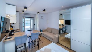 A modern, well-lit room with a wooden dining table, a sofa, and a TV.