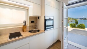 A modern kitchen with a built-in oven, a sink, and a window offering a view of the sea.