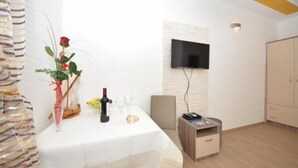 A room with a white table set for two, a TV mounted on the wall, and a wooden cabinet.