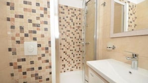 A bathroom with mosaic tile walls, a shower, a sink, and a mirror.