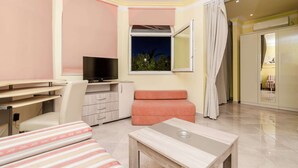 Ein modernes Hotelzimmer mit Fernseher, Schreibtisch, Sofa und einem Balkon mit Blick auf den Nachthimmel.