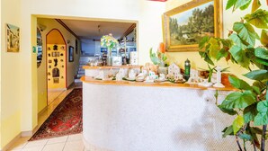Un hall d’hôtel avec un comptoir d’accueil, un escalier menant à l’étage supérieur et un tableau accroché au mur.