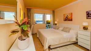 A bedroom with a bed, bedside tables, a potted plant, and a view of the outdoors.