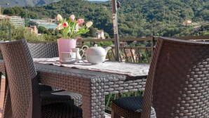 A wicker table with chairs, a vase of flowers, and a teapot on a balcony overlooking a mountainous landscape. - Apartment 'Cà Teodoi' with Sea View, Wi-Fi and Air Conditioning (Genova)