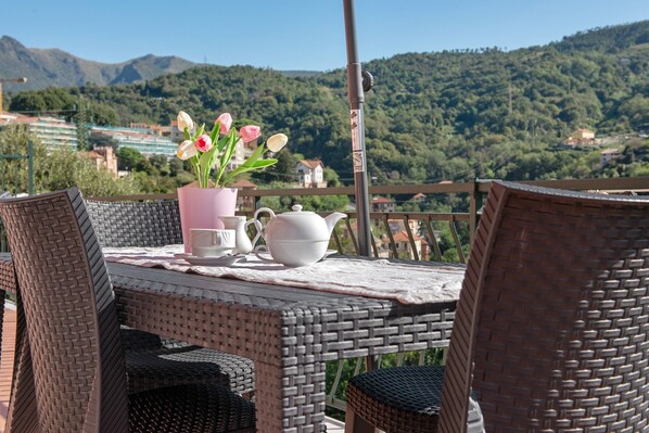 A wicker table with chairs, a vase of flowers, and a teapot on a balcony overlooking a mountainous landscape. - Apartment 'Cà Teodoi' with Sea View, Wi-Fi and Air Conditioning (Genova)