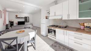 A modern kitchen with white cabinets, a gas stove, and a dining area with a table and chairs. - Apartment 'Cà Teodoi' with Sea View, Wi-Fi and Air Conditioning (Genova)