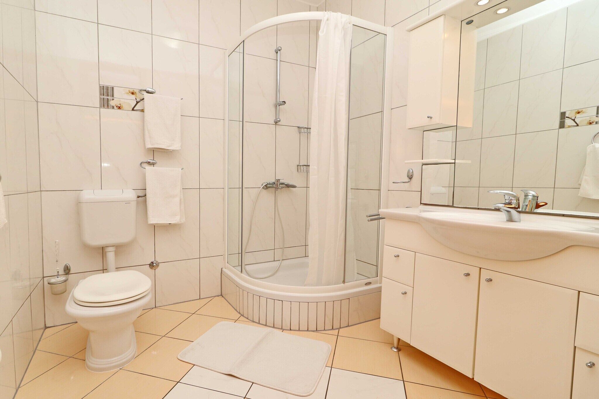 Un baño moderno con ducha envuelta en vidrio, inodoro, lavabo y espejo.