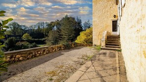 Un edificio de piedra con un sendero de grava que lleva a una puerta, rodeado de árboles y un cielo despejado.