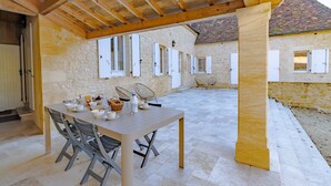 Un patio al aire libre con una mesa dispuesta para comer, rodeado de muros de piedra y vigas de madera.