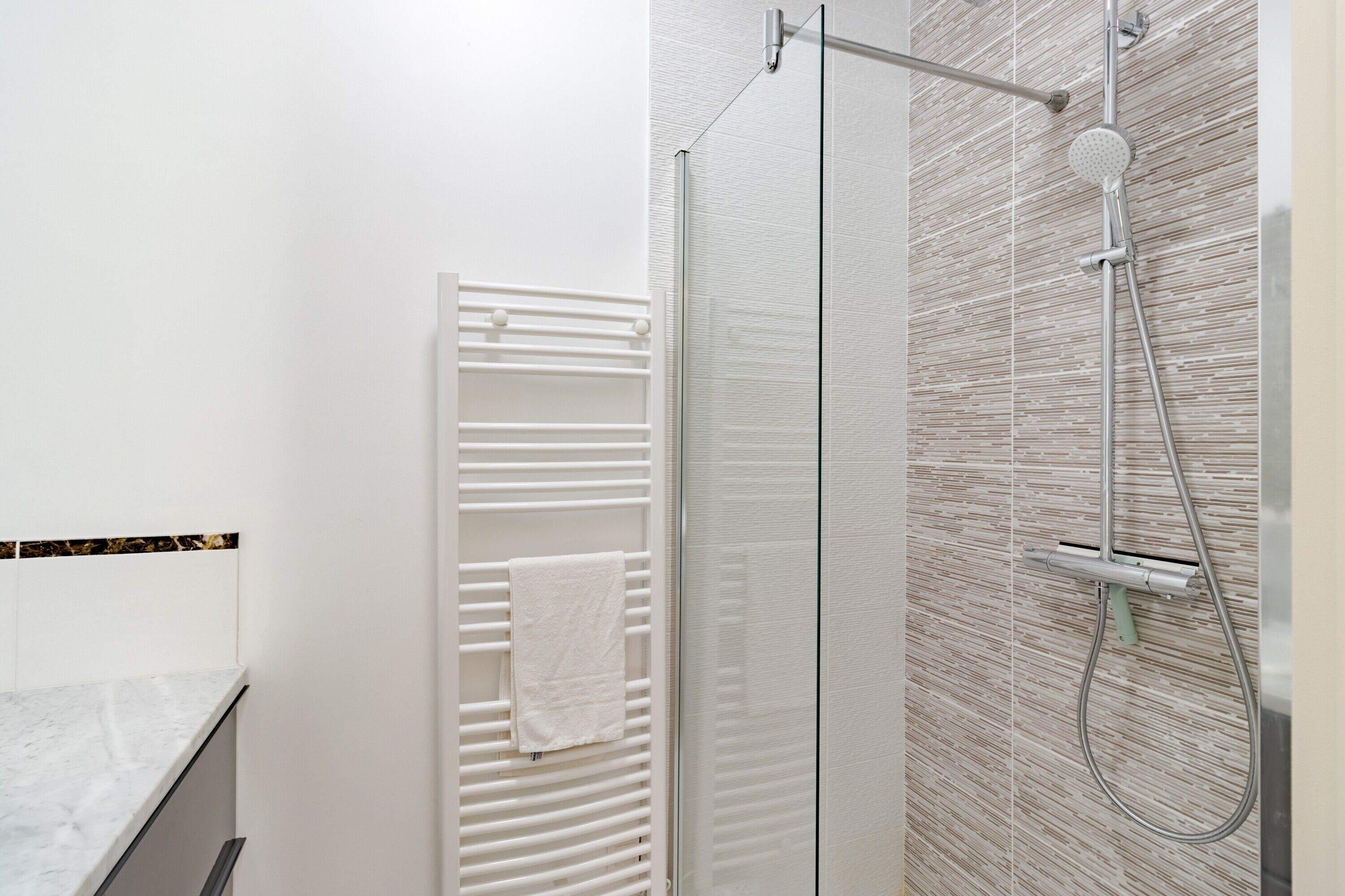 Un baño moderno con cabina de ducha de vidrio, un toallero blanco y una pared con textura.