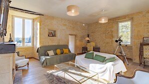 Una habitación con pared de piedra, una cama, un sofá, una silla, una mesa y un telescopio.