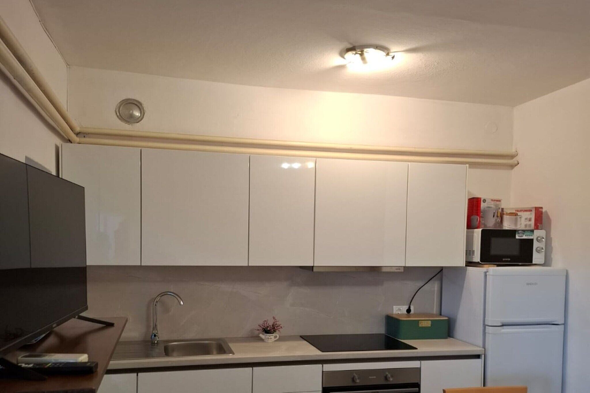 A compact kitchen with white cabinets, a stainless steel sink, a microwave, and a refrigerator.