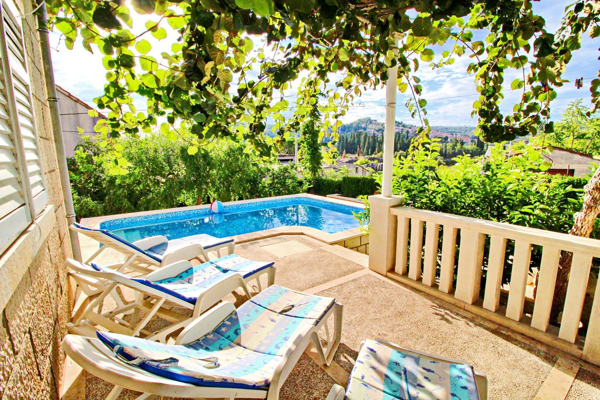 A pool area with lounge chairs and a view of a town.