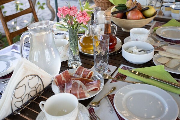 A table set for breakfast with plates, cutlery, a pitcher, a vase with flowers, and a bowl of fruit.
