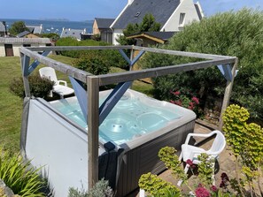Una vasca idromassaggio in un giardino con vista su case e sul mare.