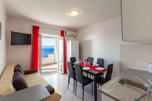 A compact room with a dining table set for two, a sofa, a kitchenette, and a TV mounted on the wall. - Apartments Nena (ST) - Two Bedroom Apartment with Terrace and Sea View (A3) (Pisak)