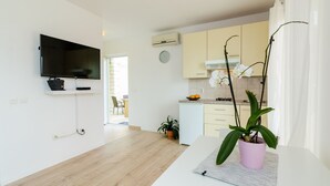 A modern living room with a flat-screen TV, a white sofa, and a potted orchid. - Color Apartments - Standard One-Bedroom Apartment with Terrace and Partial Sea View (Red) (Mlini)