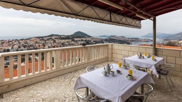 Una terraza con mesas dispuestas para comer, con vistas a un pueblo con edificios y colinas.