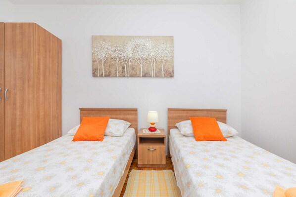 A room with two beds, a wooden wardrobe, a nightstand with a lamp, and a painting of trees on the wall. - Rooms Ivo - Twin Room with Shared Bathroom (Dubrovnik)