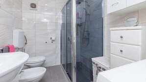 Un baño moderno con ducha envuelta en vidrio, un lavamanos blanco y un inodoro.