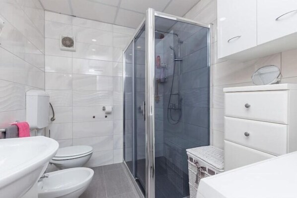 Un baño moderno con ducha envuelta en vidrio, un lavamanos blanco y un inodoro.
