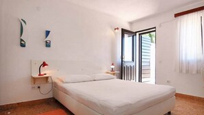 Un dormitorio con cama, una mesita de noche con lámpara, una ventana con cortinas y una puerta que da al exterior.