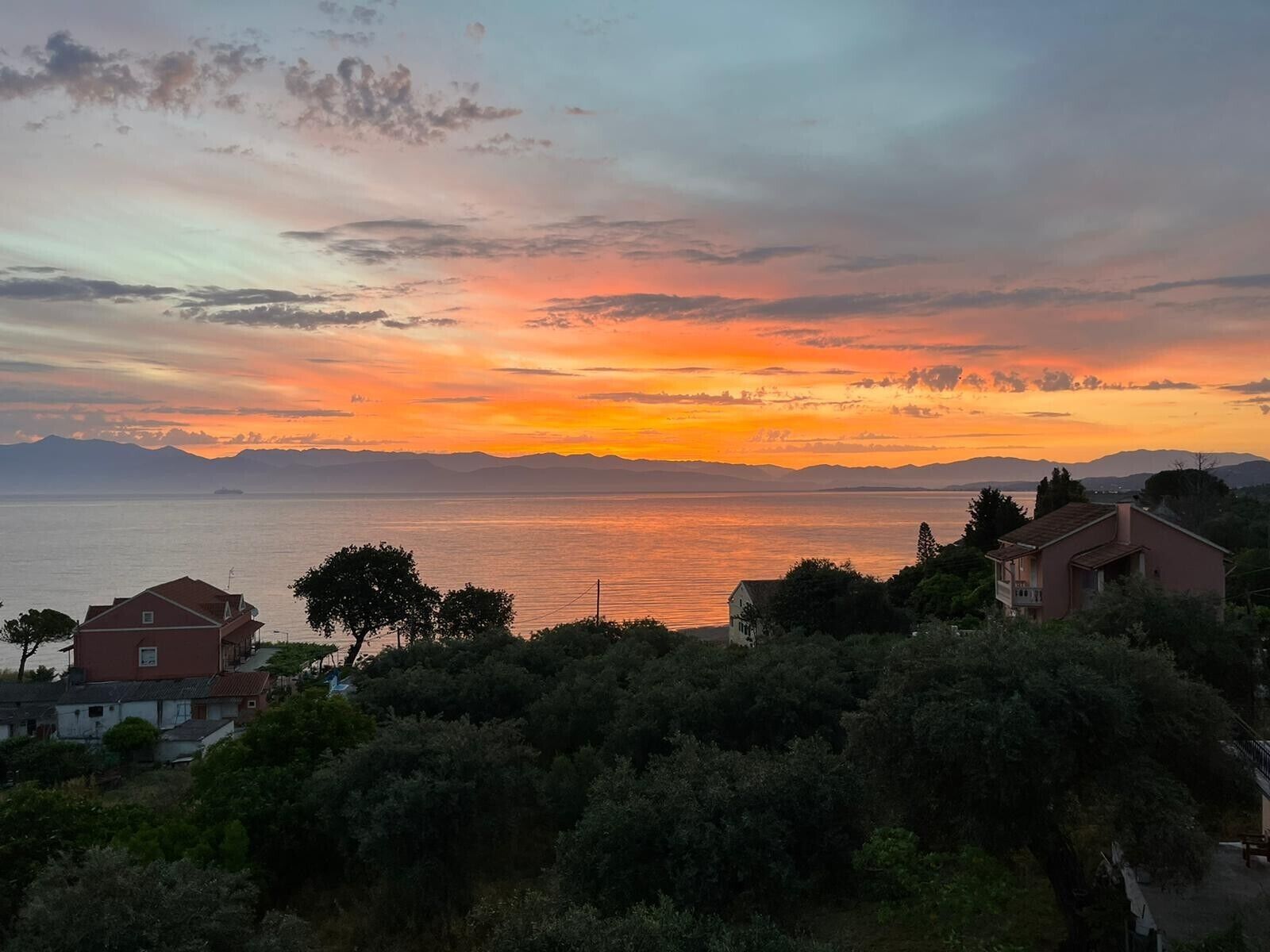 A coastal landscape with a sunset, houses, and a body of water.