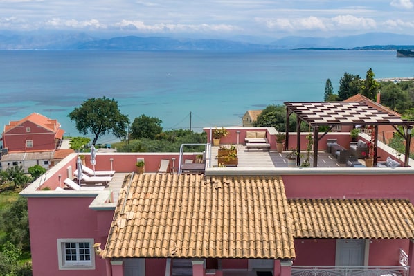 Une terrasse sur le toit dotée d’un parasol à carreaux, d’un espace salon avec des meubles d’extérieur, et offrant une vue sur la mer et les montagnes lointaines.