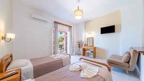 A hotel room with two beds, a desk, a chair, a TV, and an air conditioning unit. - Studio Apartment 'GRAND  4' with Sea View, Wi-Fi and Air Conditioning (Corfu)