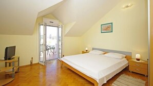 A bedroom with a large bed, a television, a desk, and a sliding glass door leading to a balcony. - Apartments Villa Rose - Economy Studio with Sea View and shared  Terrace (A3 crveni) (Sumartin)
