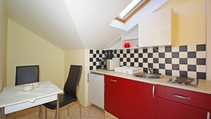 A compact kitchen with a checkered backsplash, a small refrigerator, a sink, and a dining area with a table and chairs. - Apartments Villa Rose - Economy Studio with Sea View and shared  Terrace (A3 crveni) (Sumartin)