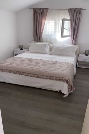 Quarto com cama, mesas de cabeceira, janela com cortinas e vista para o exterior.