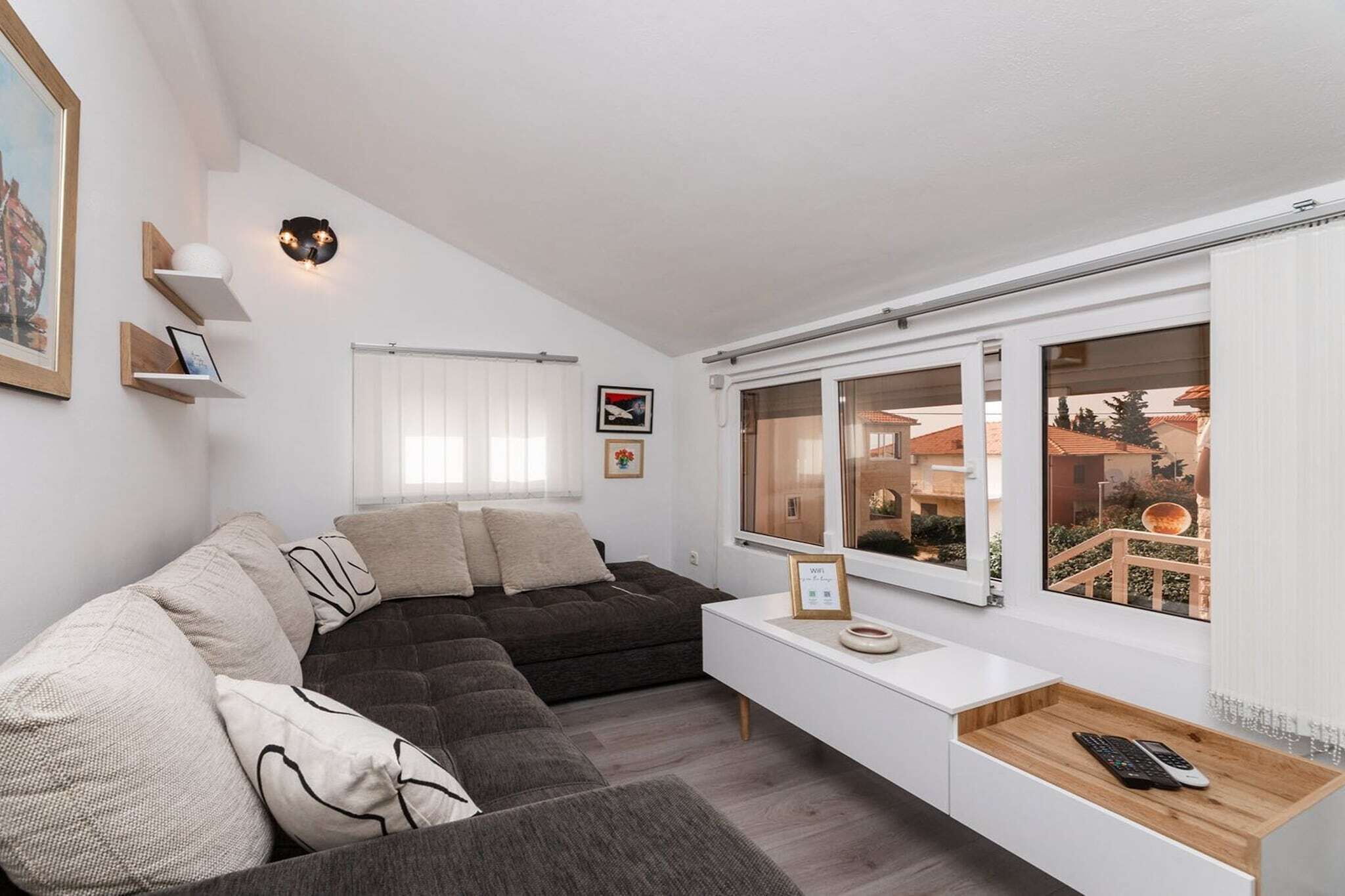 A modern living room with a sectional sofa, a white console table, a large window with a view of buildings, and a wall-mounted light fixture.