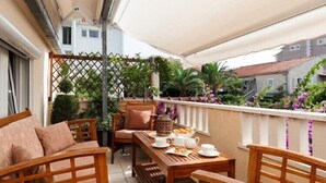 Ein Balkon mit Holzmöbeln, einem Tisch gedeckt mit Tassen und Gebäck, und Blick auf einen Garten mit Pflanzen und Blumen.