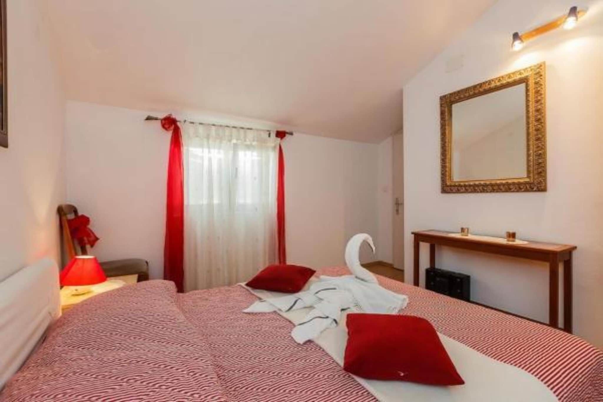 Een slaapkamer met een bed, rode gordijnen, een spiegel en een nachtkastje met een lamp.